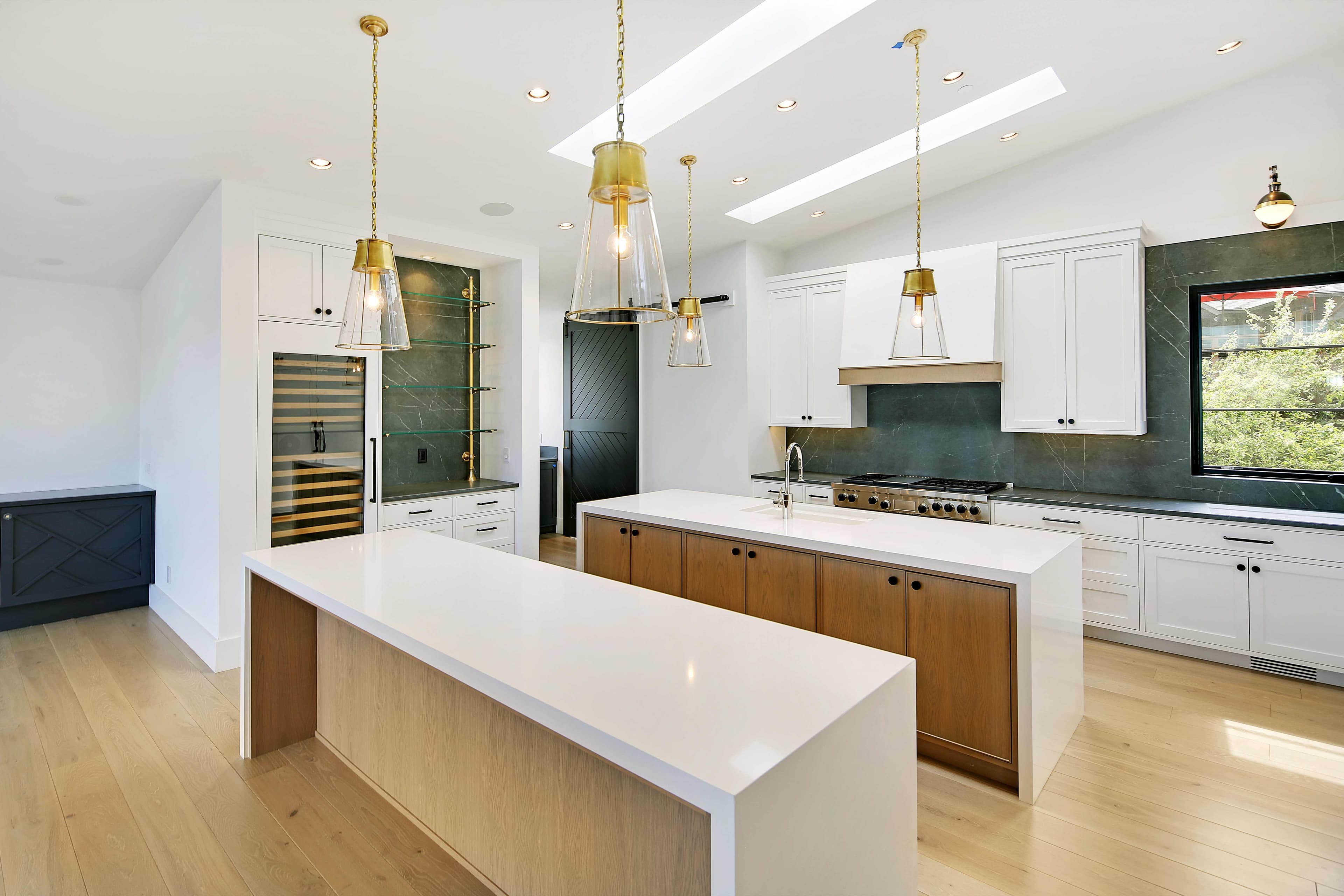 Luxury kitchen design by ID by Gwen featuring white cabinetry, dual islands, green marble backsplash, and brass pendant lighting in Mercer Island home